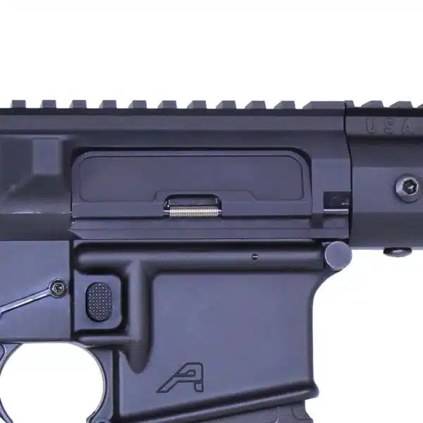 Close-up of matte black AR-style rifle receiver with Picatinny rail and forward assist button.