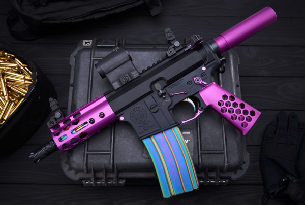 Custom pink and black firearm with striped magazine and tactical accessories on dark case.