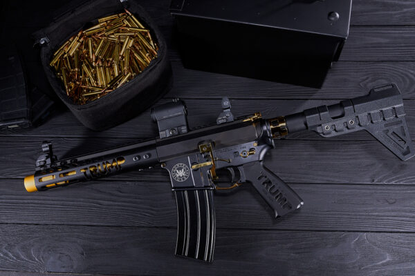 Luxurious black and gold assault rifle with ammunition on a wooden surface.